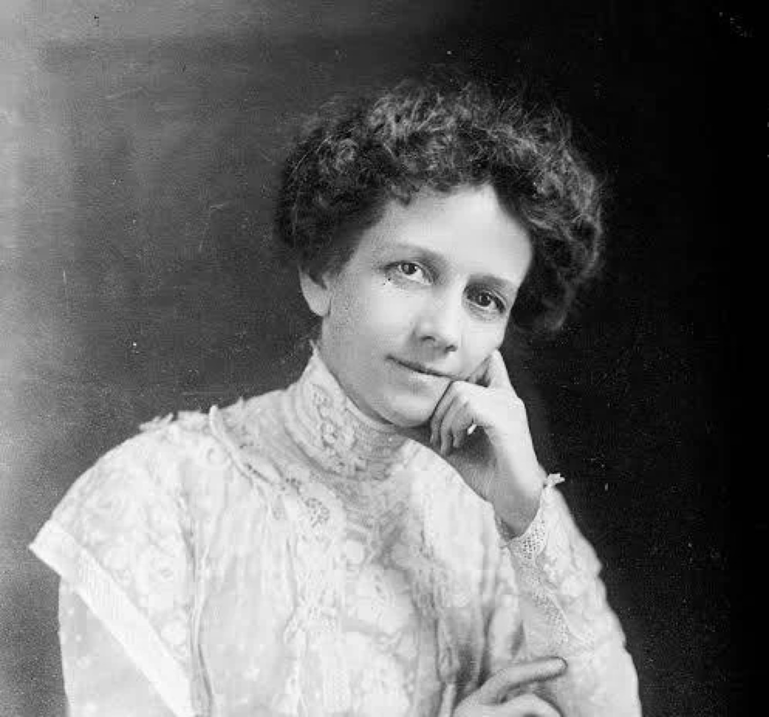 Black-and-white studio portrait of Albion Fellows Bacon, wearing a high-collared lace dress, chin resting on her hand.
